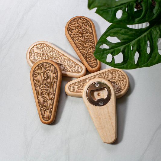 Wooden bottle openers with leaf pattern on a light surface with a leaf in the background