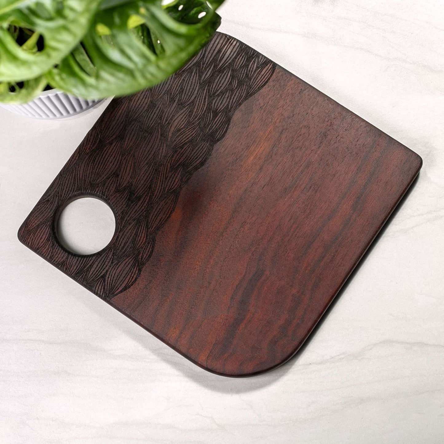 Wooden cutting board with a plant in the background on a white surface