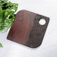 Wooden cutting board with a circular hole on a white surface with green leaves.