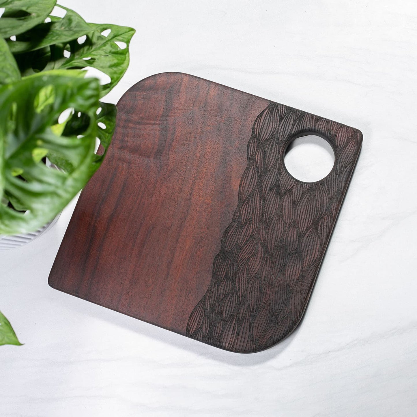 Wooden cutting board with a circular hole on a white surface with green leaves.