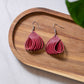 Pink teardrop earrings on a wooden tray with a light background