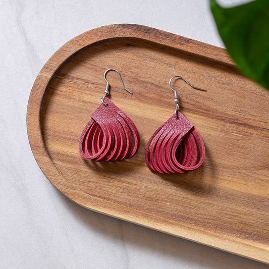 Pink teardrop earrings on a wooden tray with a light background