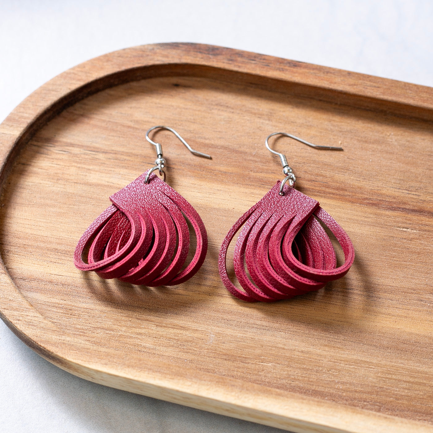 Red leather earrings on a wooden tray